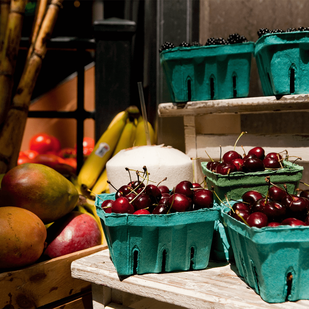 a photo of cherries, blackberries, mangos, and bananas for sell at Grove Arcade. The Cherries are in the foreground.