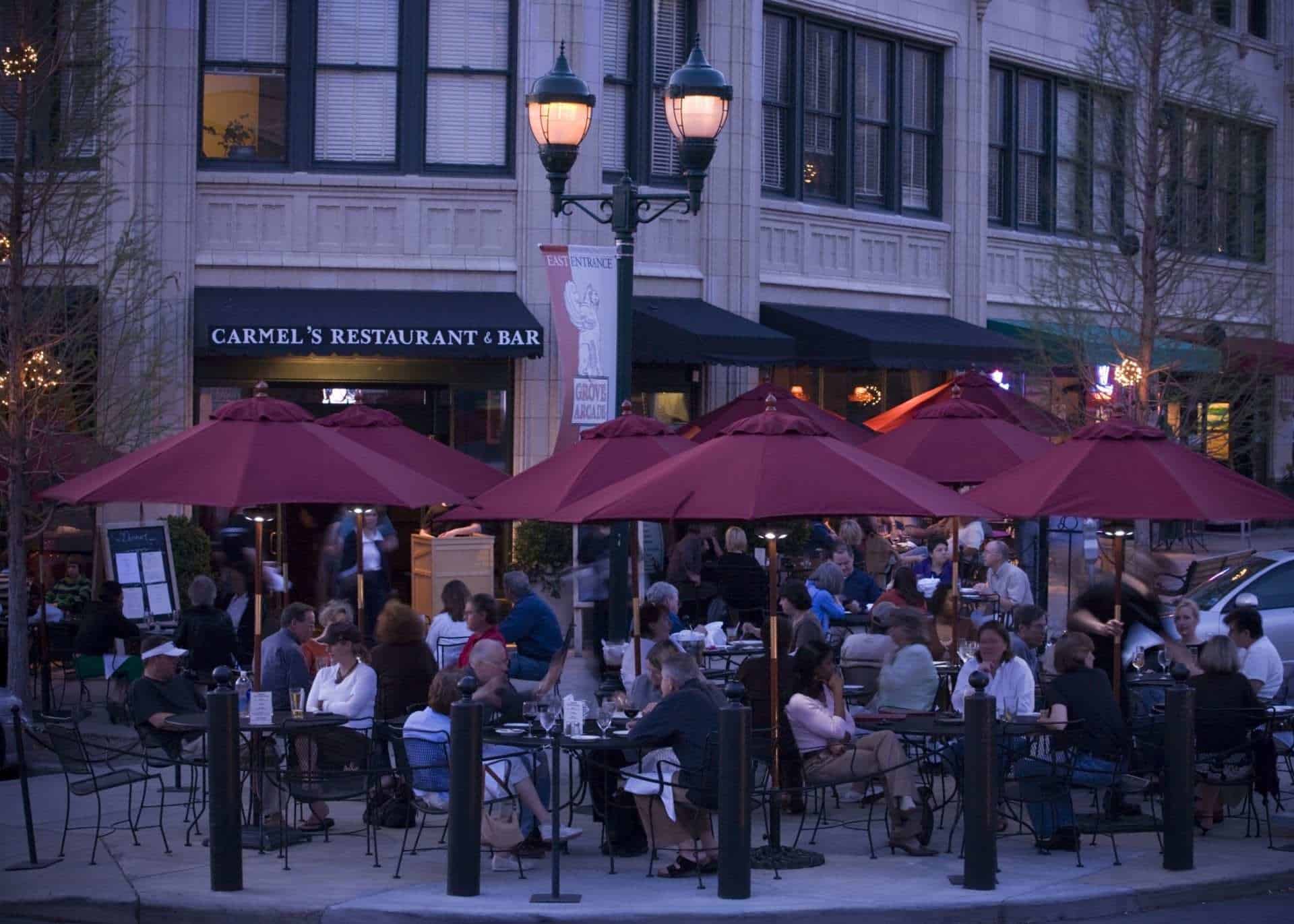 Exterior shot of Grove Arcade, where people are dining outside of Carmel's in the evening