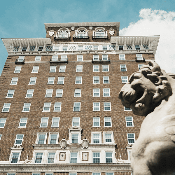 an exterior low angle shot of the battery park hotel outside of the northern entrance of the Grove Arcade, there is a winged lion in the foreground