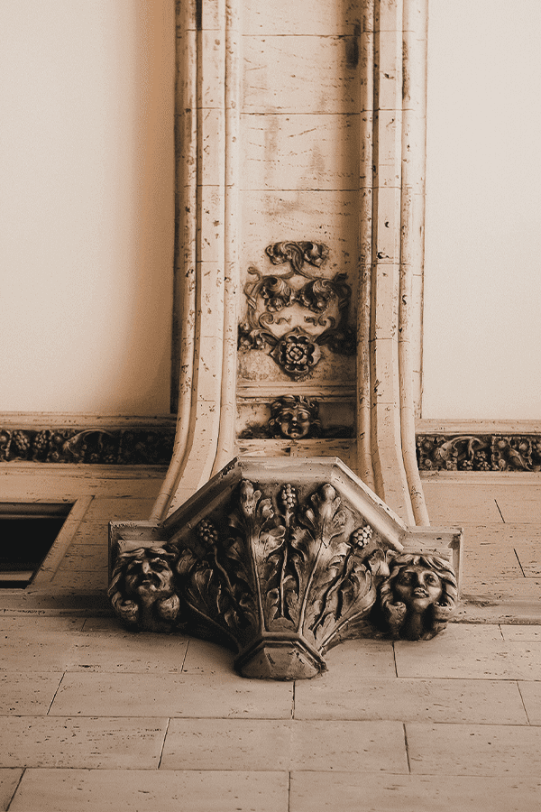 a shot looking up at some of the intricate designs featured throughout the arcade. There are two grotesque faces next to a canopy like feature with flowers carved in. the design continues onto the roof