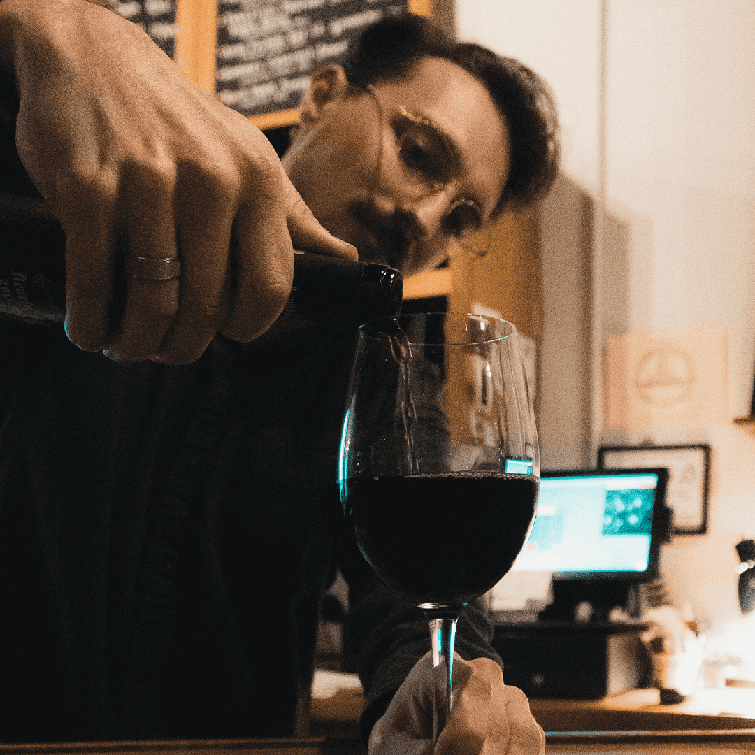 a photo of a male employee at sante pouring a glass of red wine.