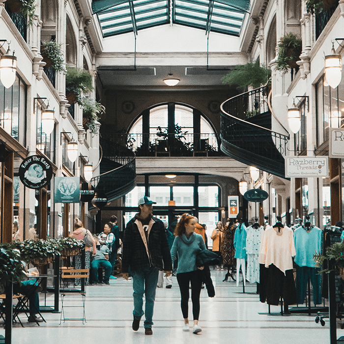 a wide shot of the inside of the grove arcade, there is a man and woman holding hands and walking through the arcade towards the camera